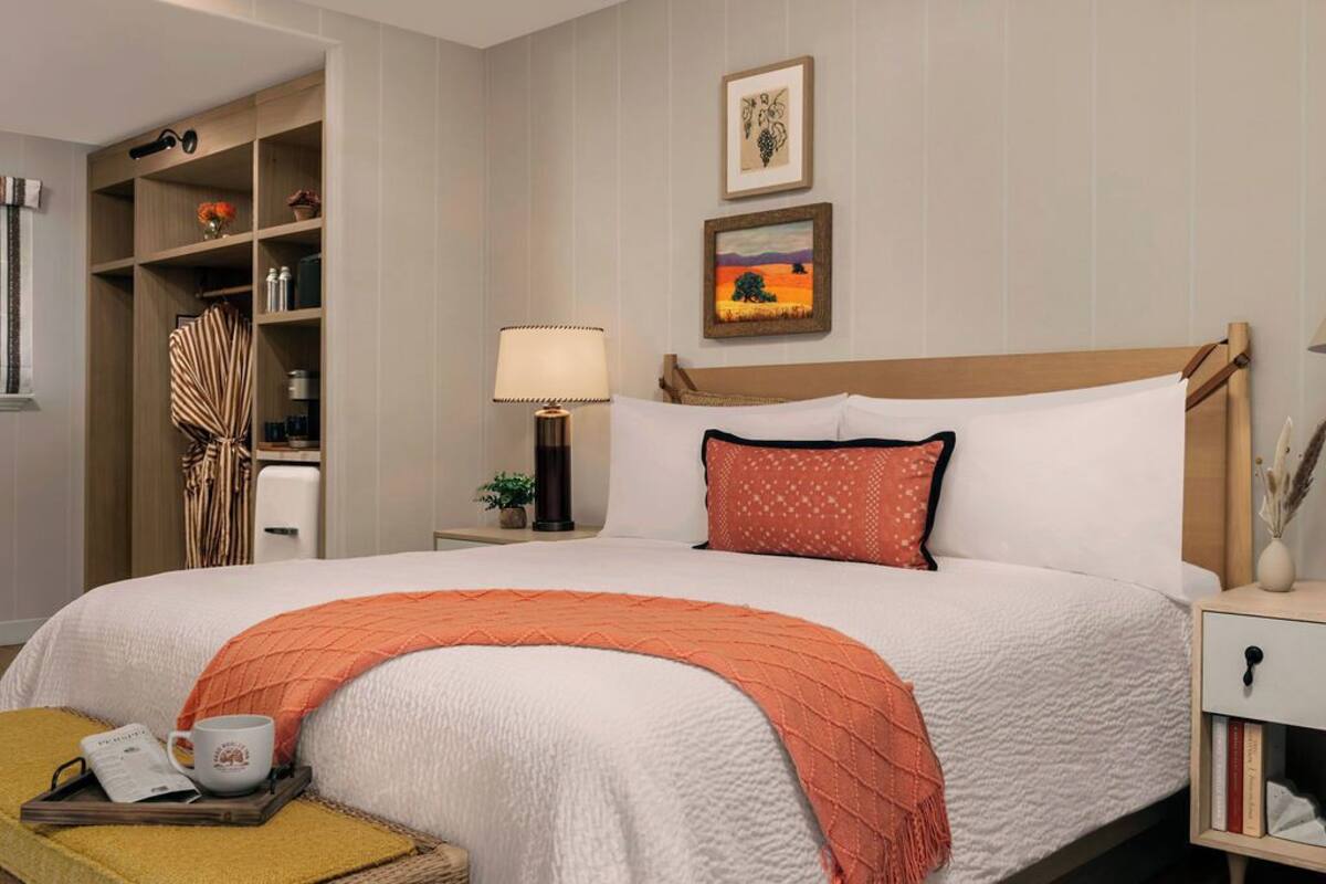 A neatly arranged hotel room with a large bed, a bedside table, a nightstand, a wardrobe, and a small table with a lamp.