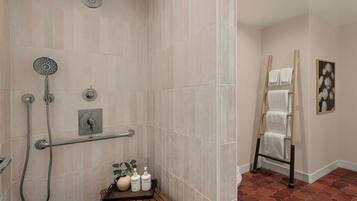 A bathroom with a shower, a towel rack, a wooden shelf with toiletries, and a tiled floor.
