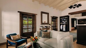 A living room with a sofa, armchair, and coffee table. There is a bookshelf and a mirror on the wall.
