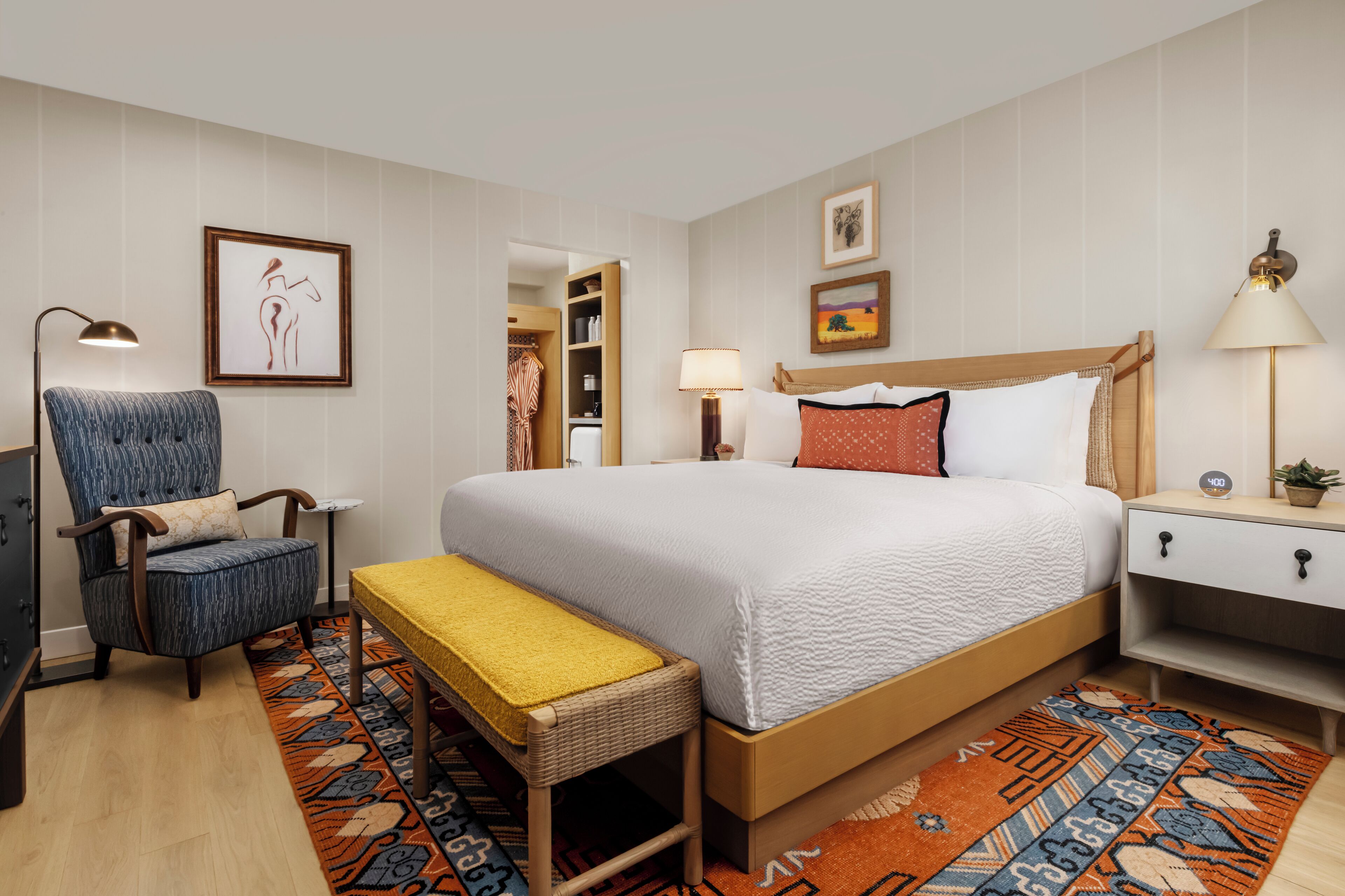 A hotel room with a bed, a chair, a bedside table, a lamp, and a rug.