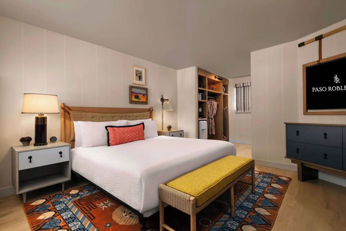 A neatly arranged hotel room with a bed, bedside tables, a bench, a wardrobe, and a TV mounted on the wall.