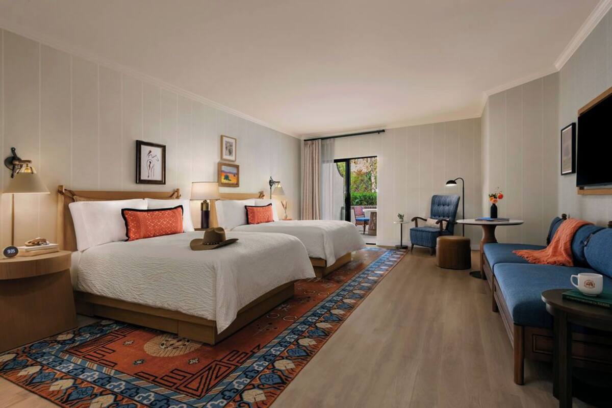 A hotel room with two beds, a sofa, a small table, and a TV.