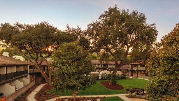 A landscaped outdoor area with a fire pit and seating, surrounded by trees and a well-maintained lawn.