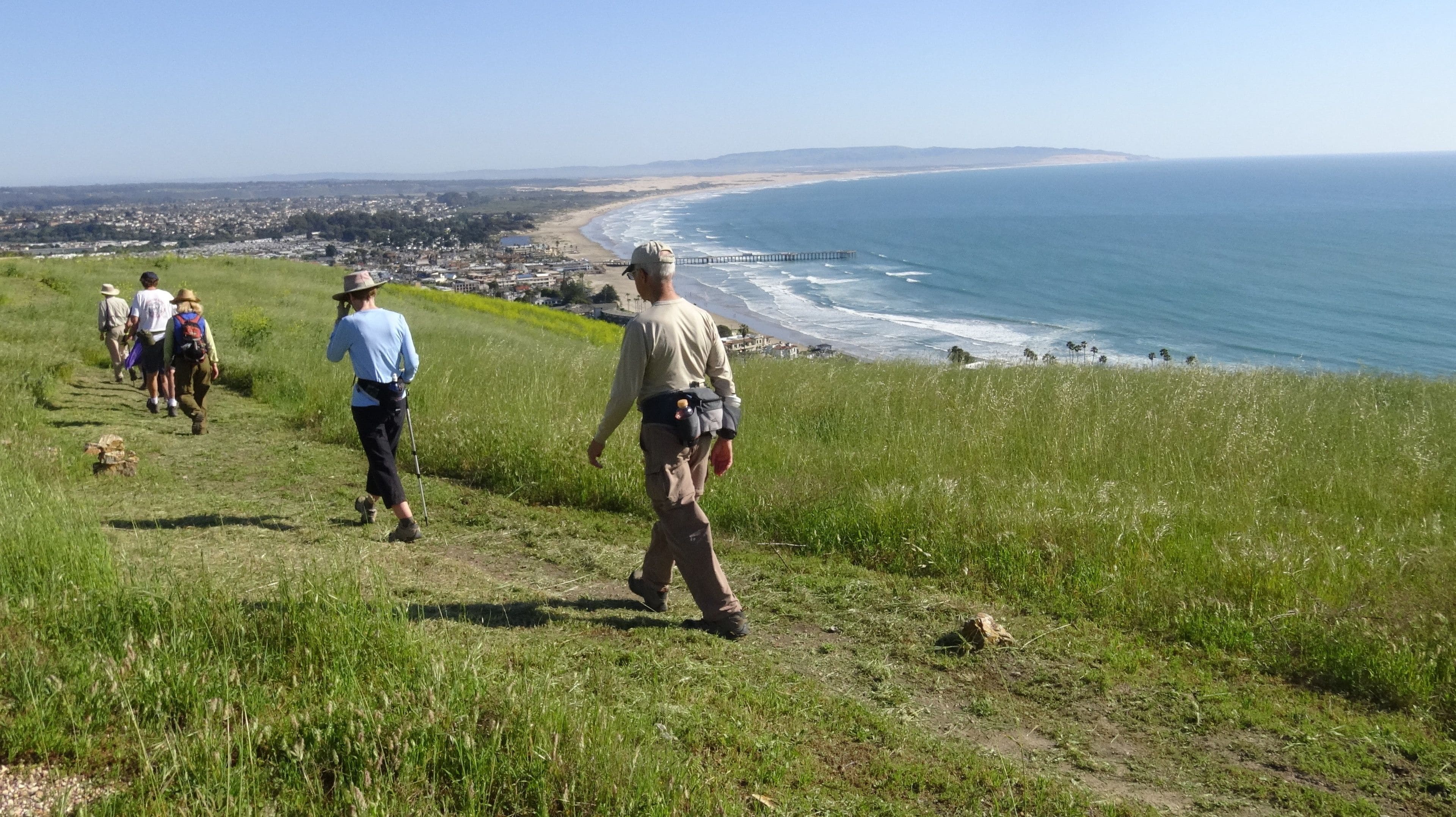 A coastal hiking trail with a view of the ocean and a beach in the distance.