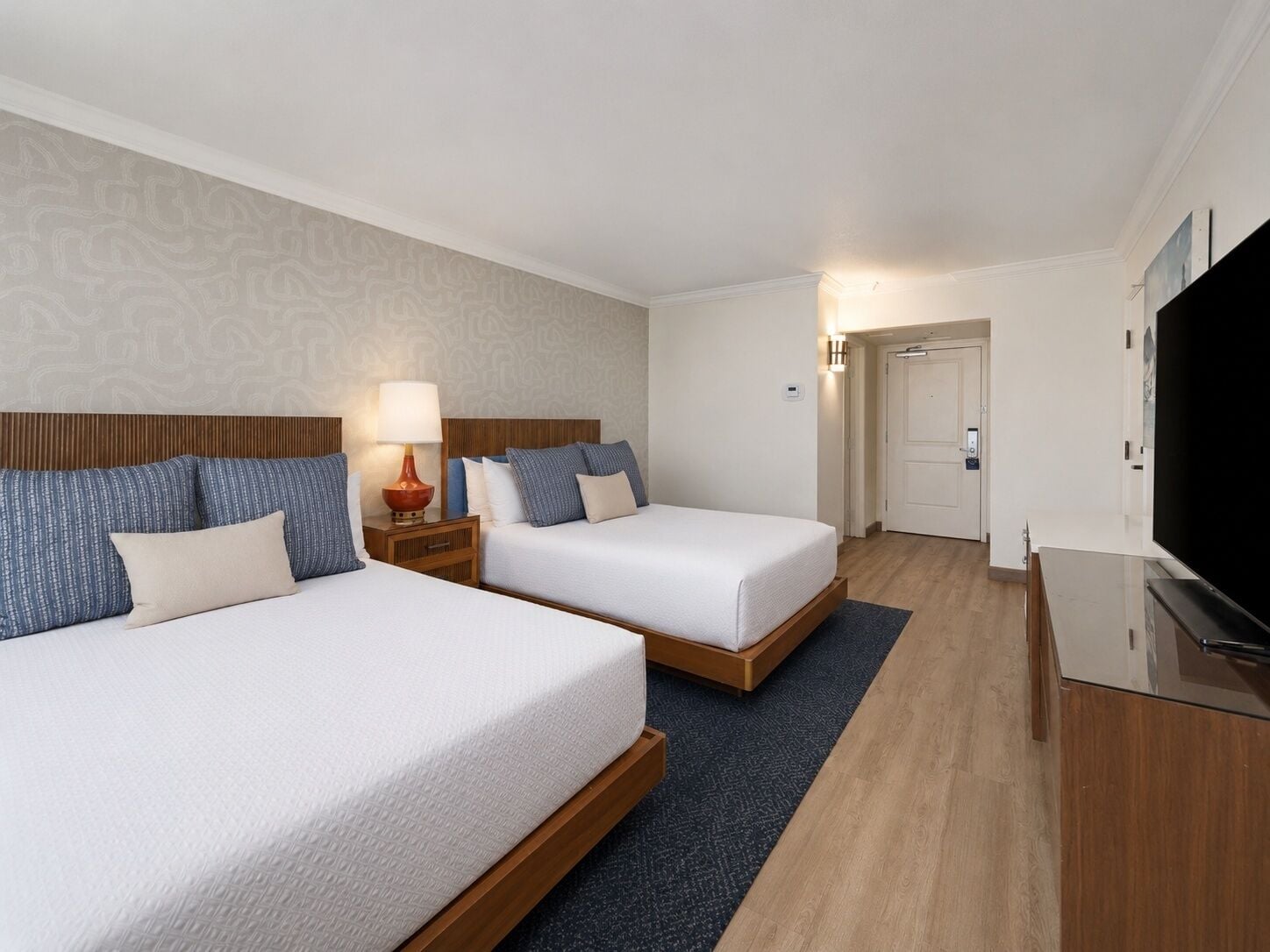 A hotel room with two beds, a television, and a door leading to a hallway.