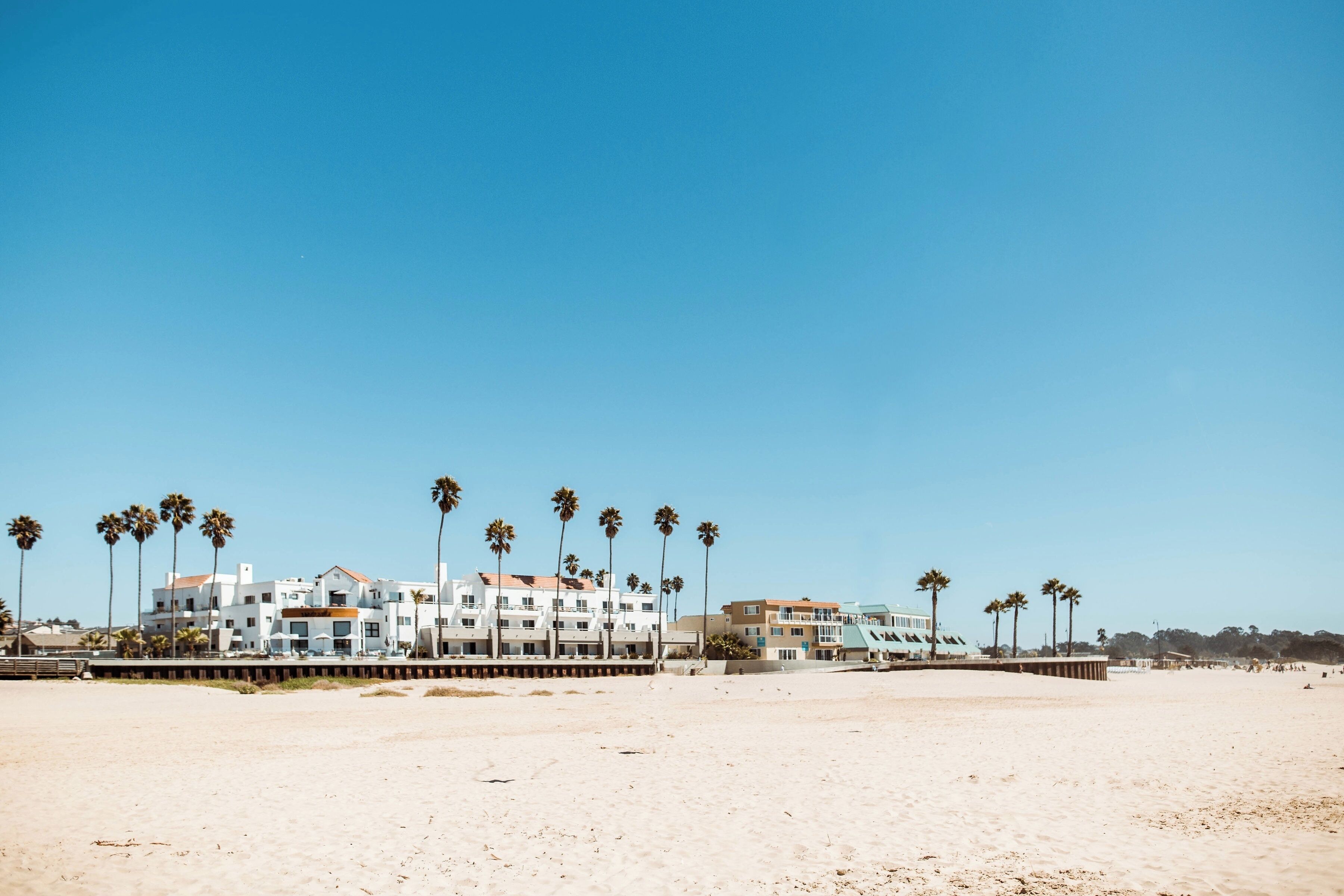 A beachfront hotel with multiple buildings, palm trees, and a sandy beach.