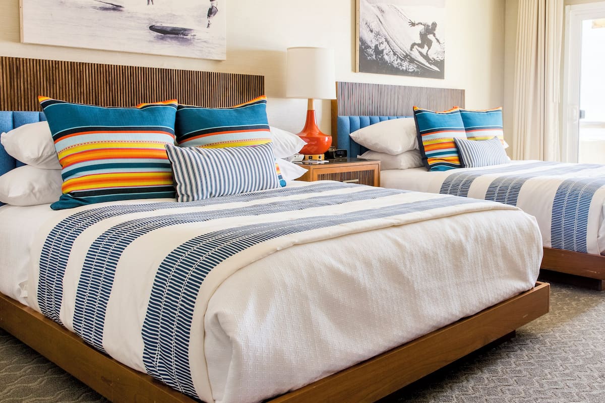 A hotel room with two beds, striped bedding, a wooden headboard, a nightstand with a lamp, and artwork on the walls.