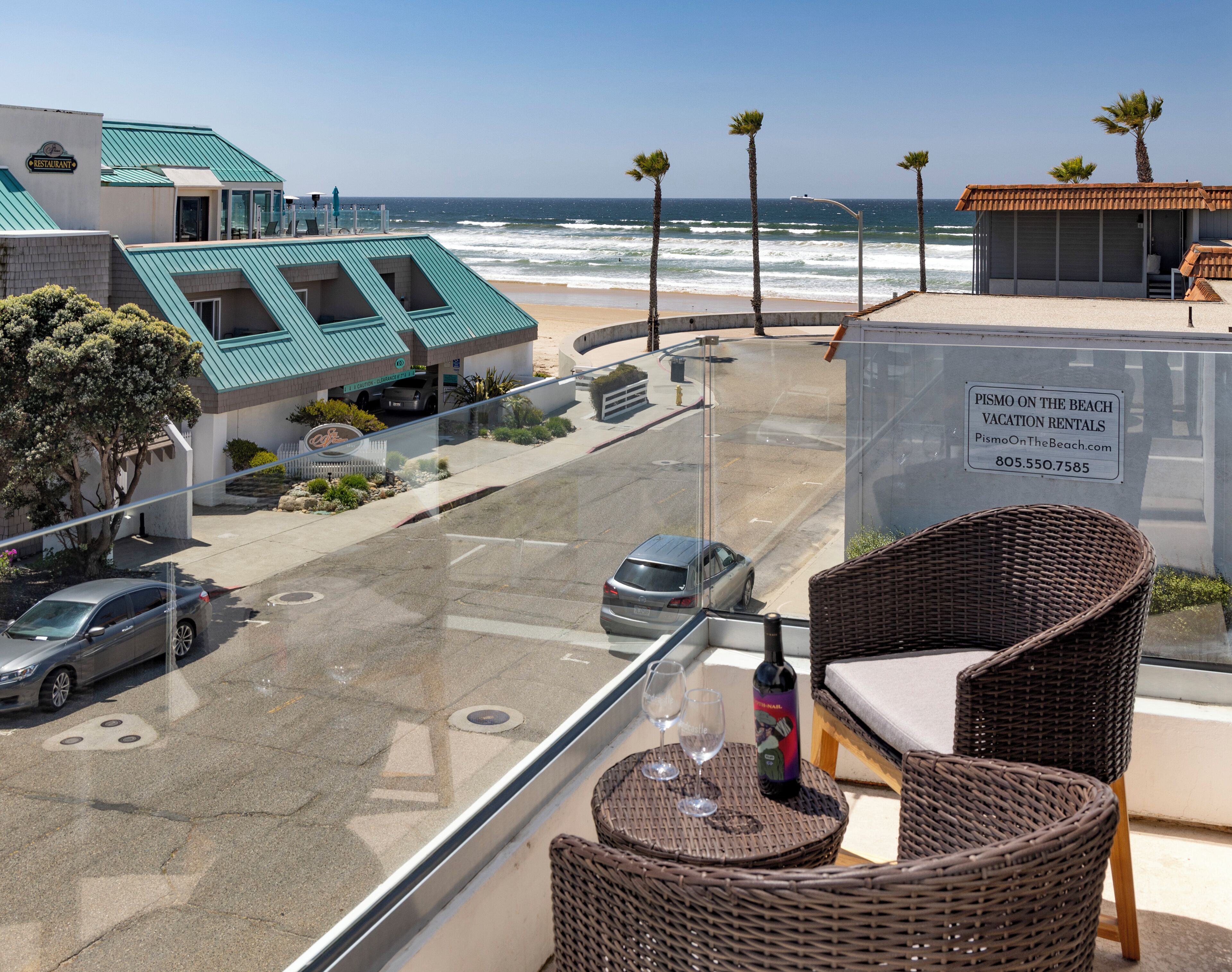A balcony with wicker furniture overlooking a beach and a parking area.