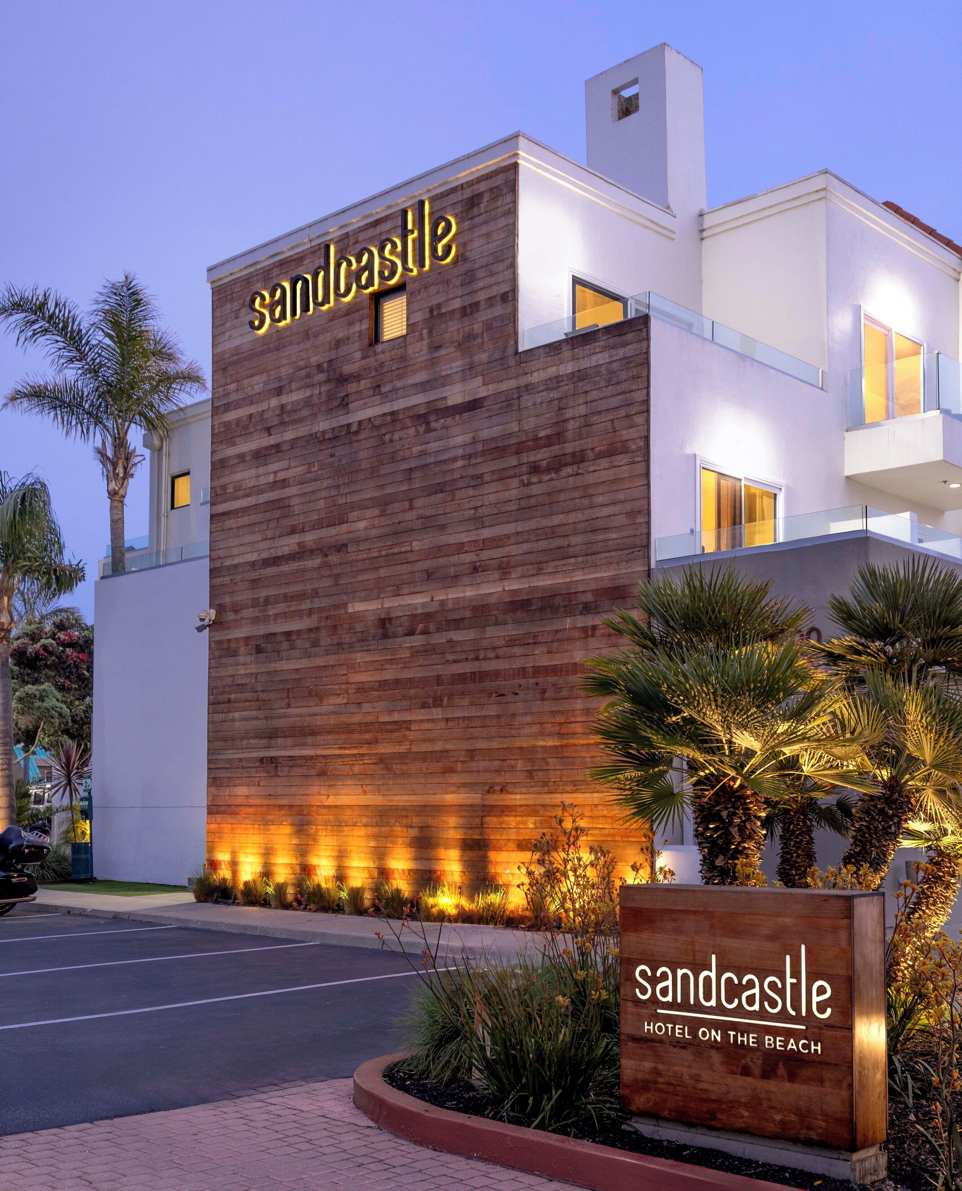 A modern hotel building with a prominent 'sandcastle' sign, featuring a wooden facade and illuminated windows.