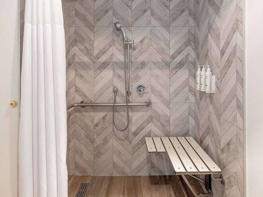 A shower area with a herringbone-patterned wall, a showerhead, a handheld shower, a bench, and a set of toiletries.