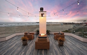 Un lounge en la azotea con una chimenea, muebles de mimbre y vistas a la playa y el muelle.