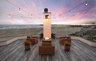 Un lounge en la azotea con una chimenea, muebles de mimbre y vistas a la playa y el muelle.