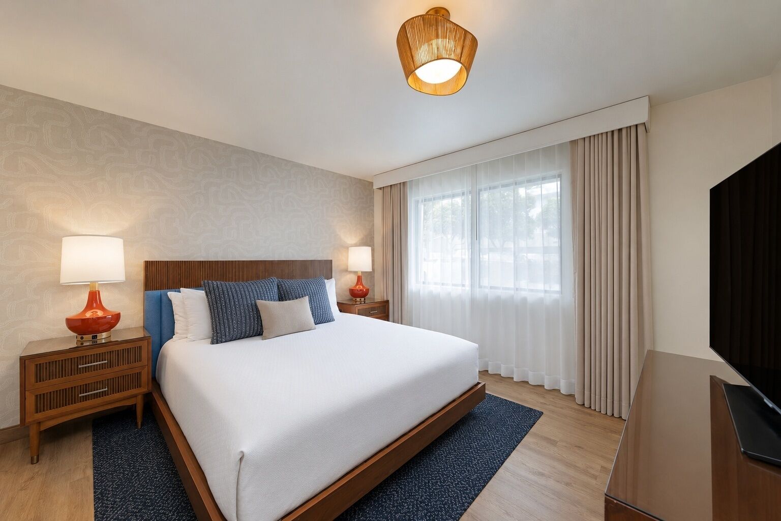 Een hotelkamer met een groot bed, twee nachtkastjes, een televisie en een raam met gordijnen.