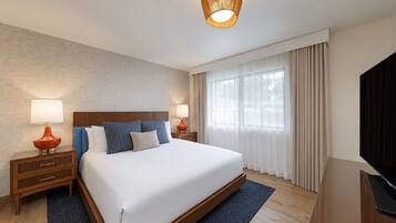 Une chambre d’hôtel avec un grand lit, deux tables de chevet, une télévision et une fenêtre avec des rideaux.