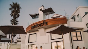 Un edificio moderno con un letrero que dice "sandcastle" y terraza al aire libre con sombrillas.
