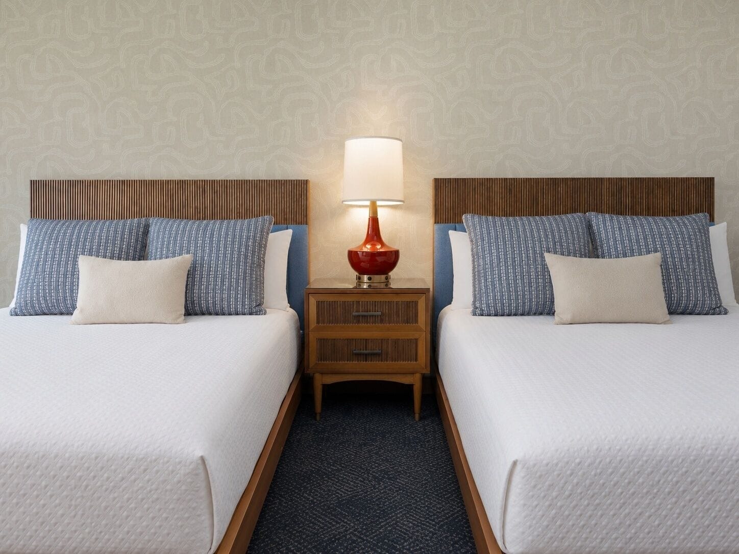 Une chambre d’hôtel avec deux lits, une table de chevet avec une lampe et un mur décoré d’un motif.