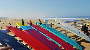 Diversas pranchas de surf alinhadas em um banco de madeira na praia.