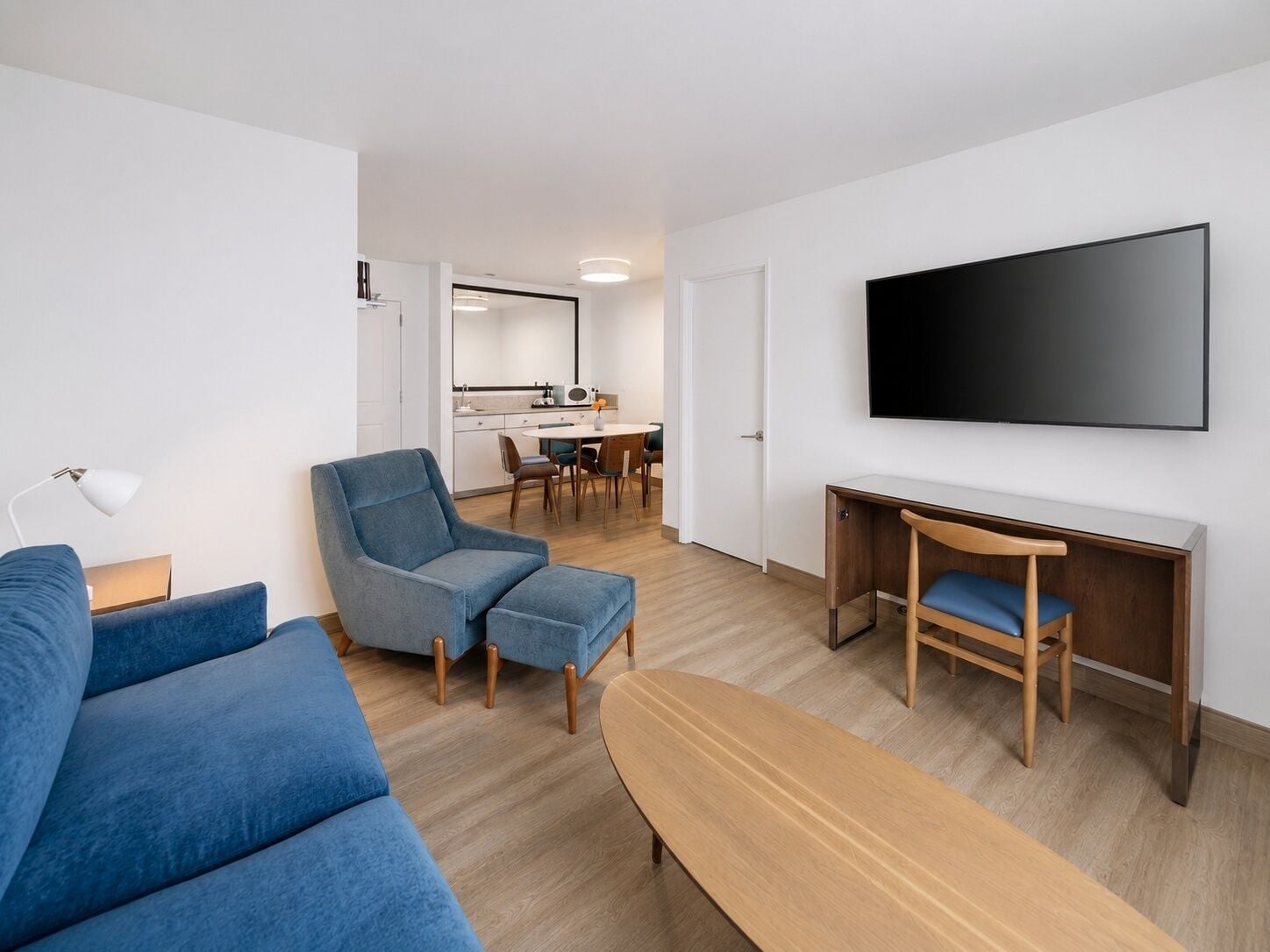 A modern living room with a sofa, a chair, a desk, and a flat-screen TV mounted on the wall.