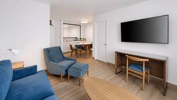 A modern living room with a sofa, a chair, a desk, and a flat-screen TV mounted on the wall.