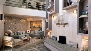 Una sala moderna con un sofá, una mesa de centro y una pared decorada con fotografías. Se observa una estantería de madera con objetos decorativos y una lámpara colgante.