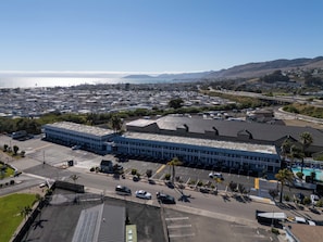 An aerial view of a commercial area with a large blue building, parking lots, and a road leading to a body of water. - The Grove At Pismo Beach (Pismo Beach)
