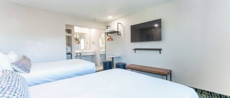 A hotel room with two beds, a TV mounted on the wall, and a small bench.