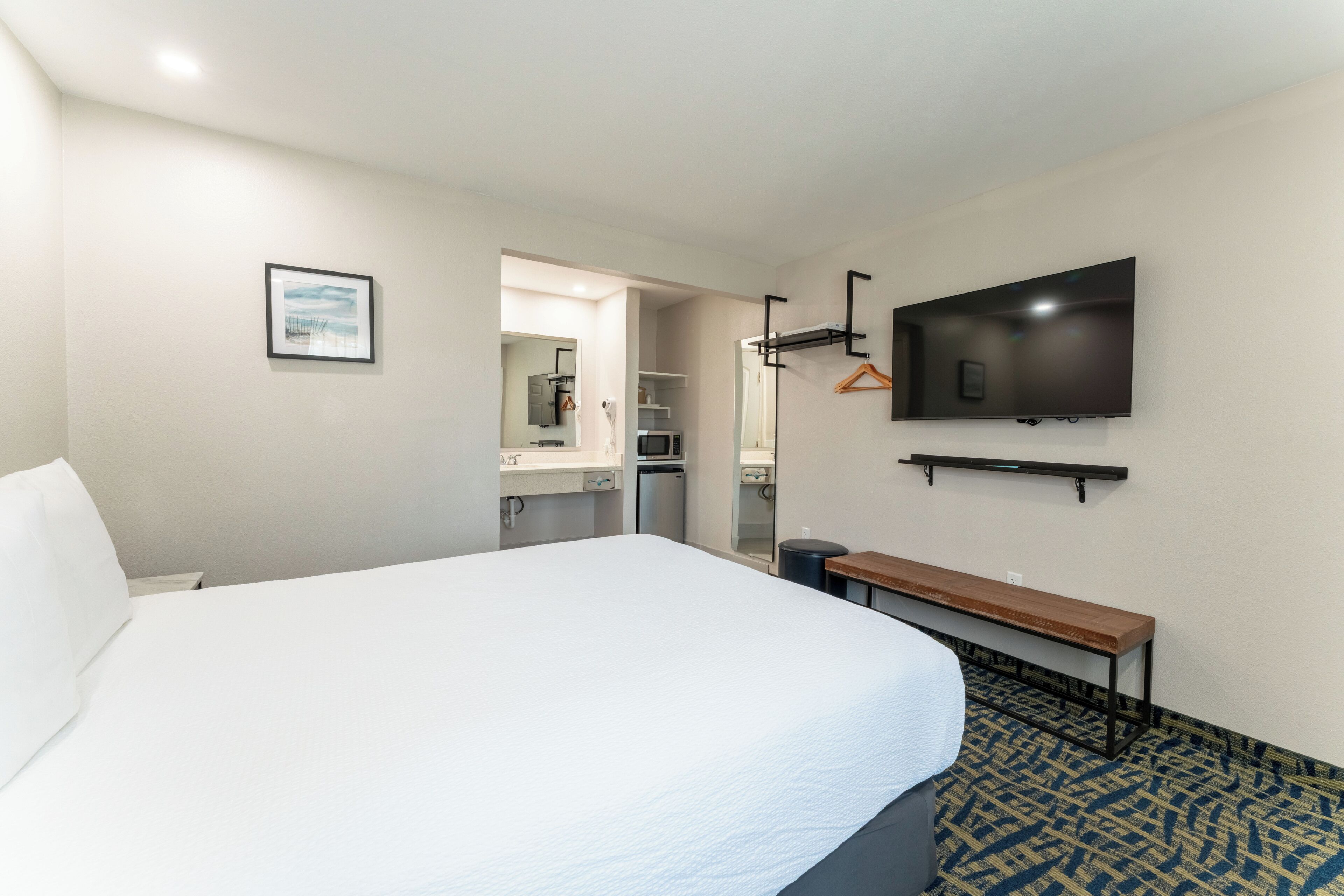 A hotel room with a large bed, a television mounted on the wall, a bench, and a patterned carpet.