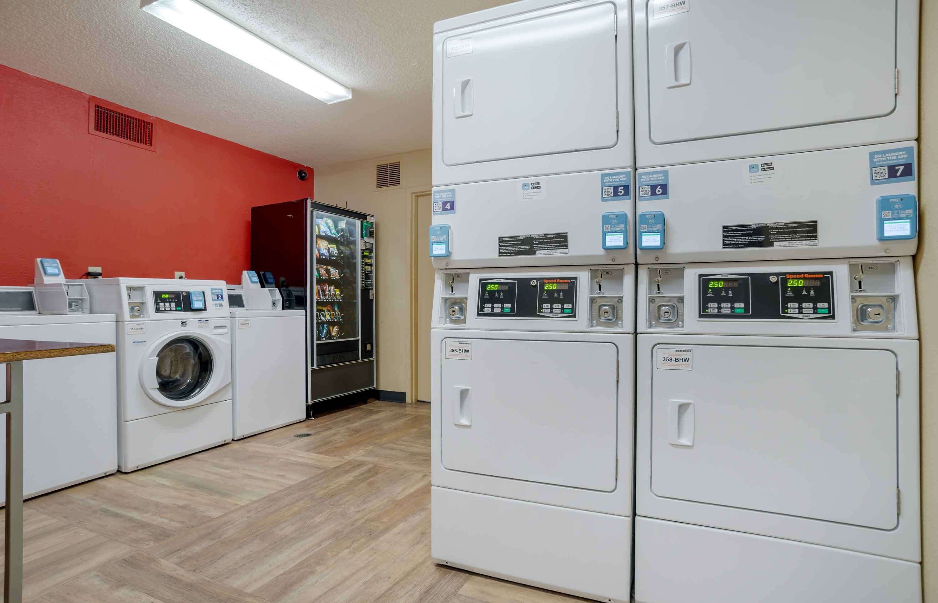A laundry facility with multiple washing machines and dryers, a vending machine, and a water cooler.