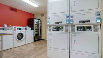A laundry facility with multiple washing machines and dryers, a vending machine, and a water cooler.