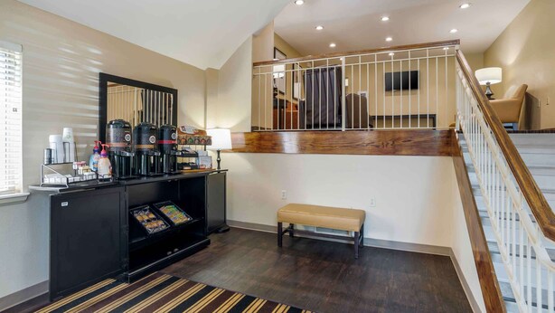 A hotel lobby with a reception desk, coffee machines, a bench, and a staircase.