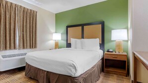 A hotel room with a large bed, two bedside tables with lamps, a heater, and a green accent wall.