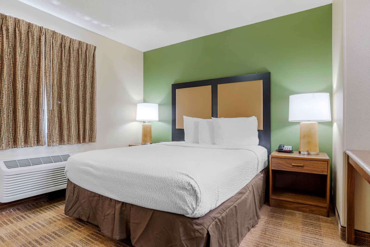 A hotel room with a large bed, two bedside tables with lamps, a heater, and a green accent wall.