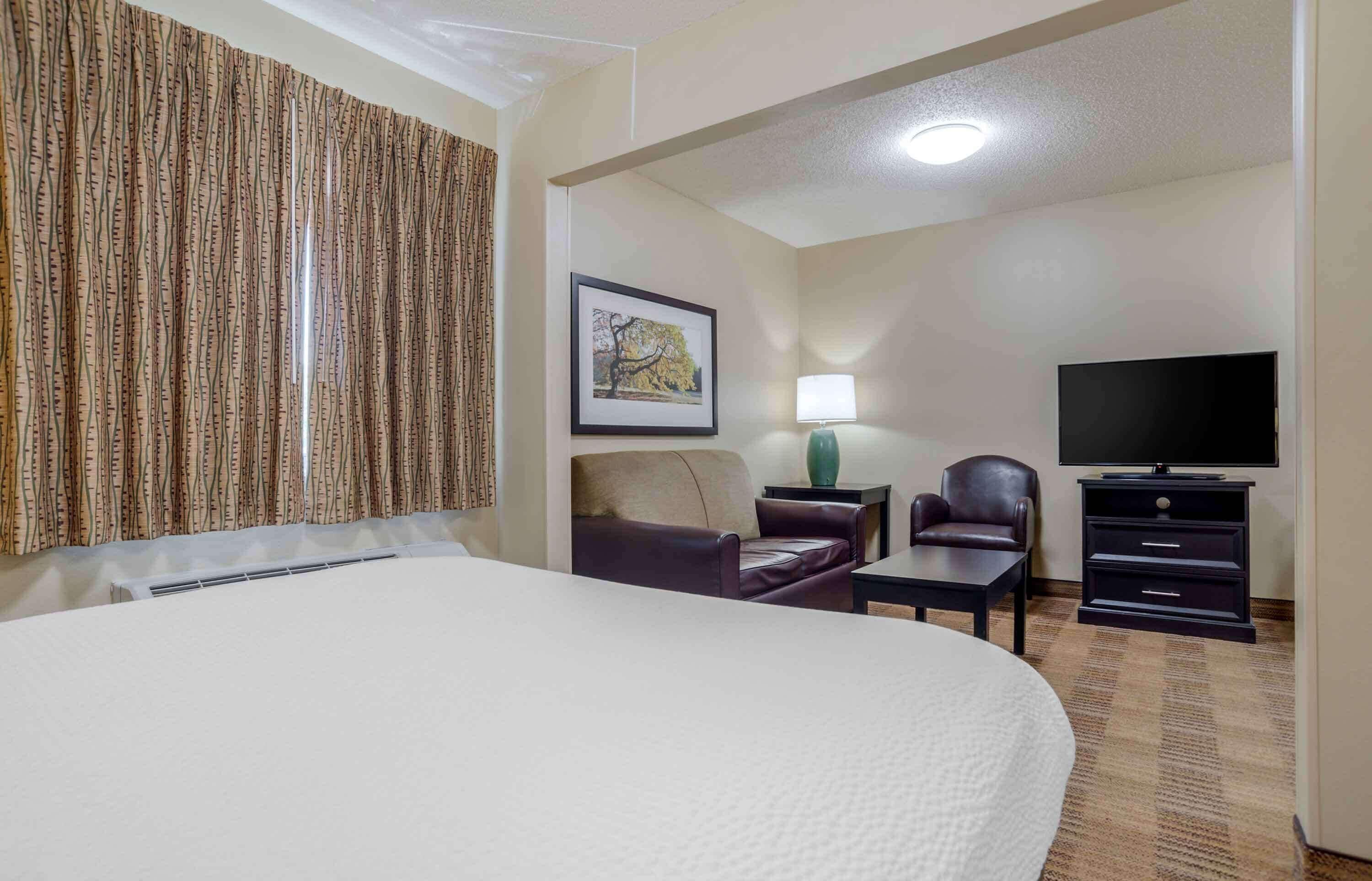 A hotel room with a large bed, a desk, a chair, a TV, and a lamp.
