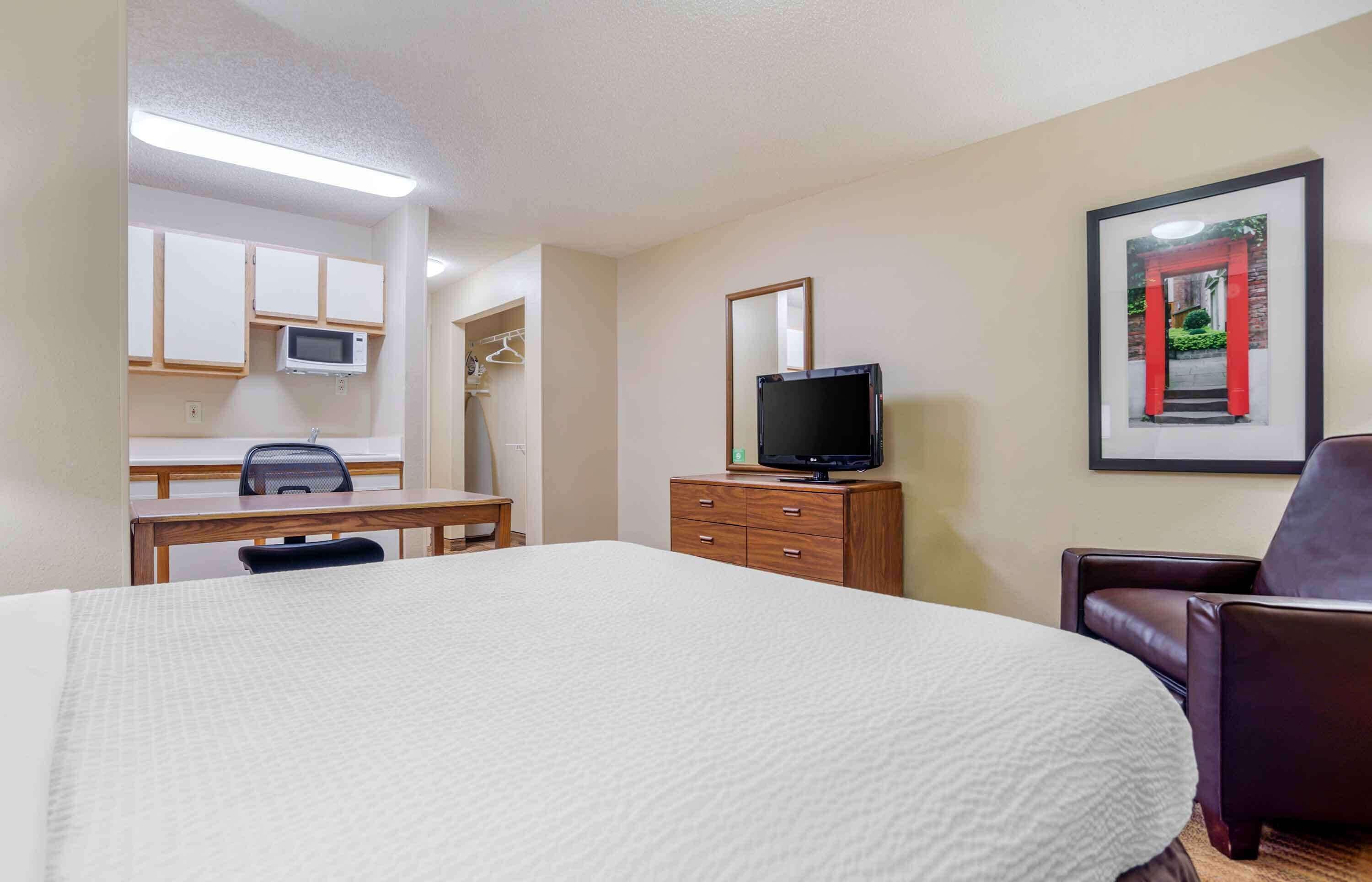 Une chambre d’hôtel avec un grand lit, un bureau avec une chaise, une télévision, une armoire et un tableau encadré au mur.