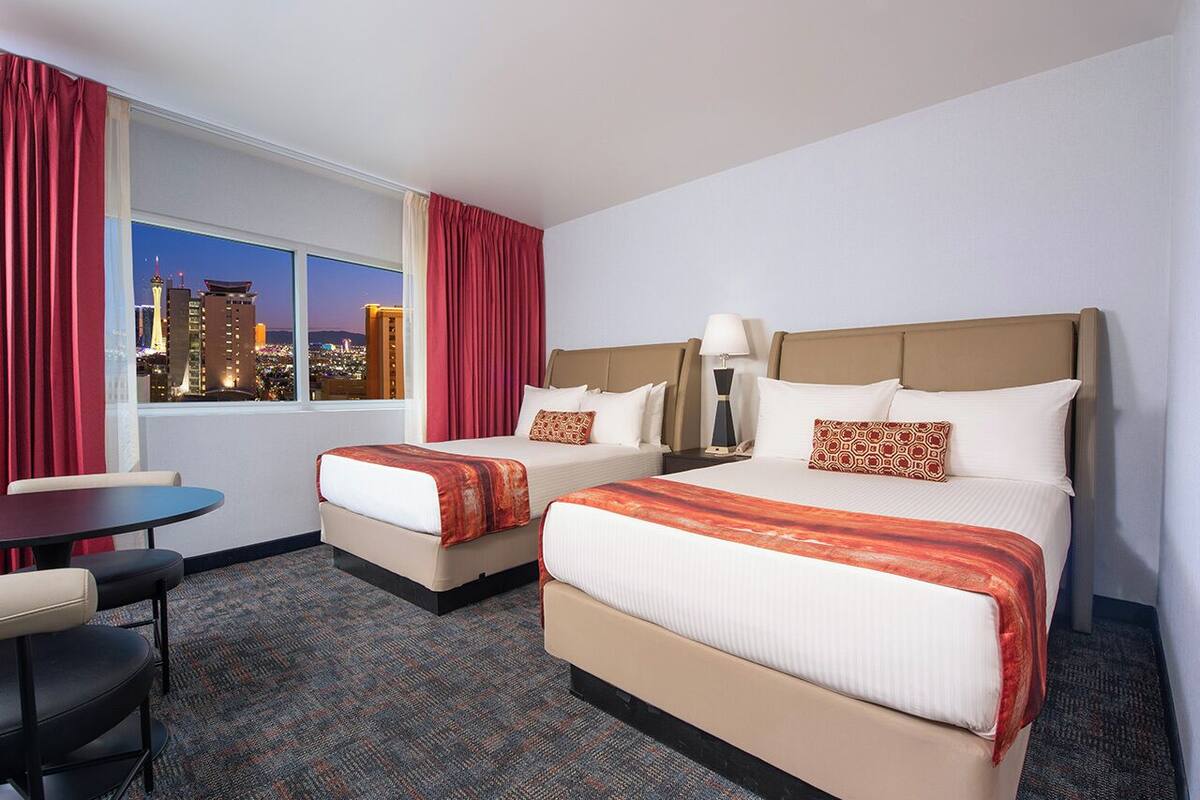 Een hotelkamer met twee bedden, een tafeltje en uitzicht op een stadsbeeld bij nacht.