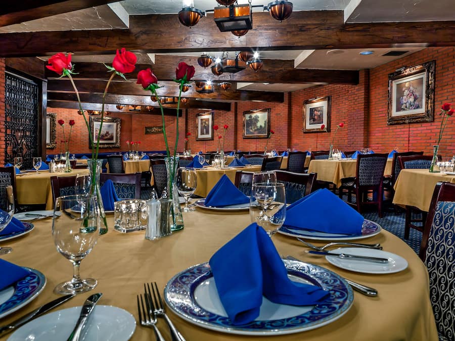 Een restaurant met gedekte tafels, blauwe servetten en rode rozen.