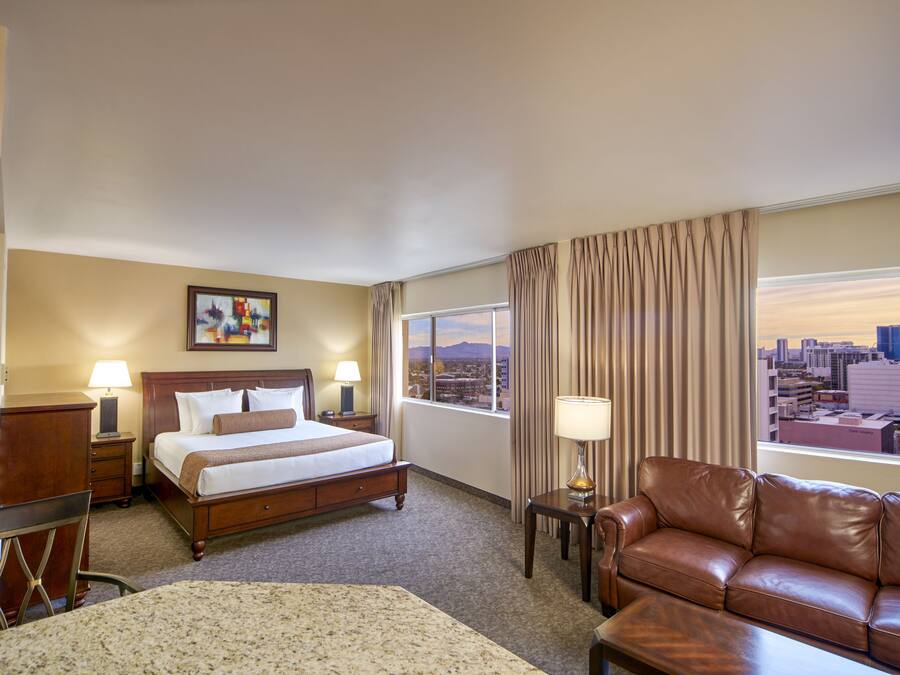 A hotel room with a bed, a brown leather sofa, a desk, and a window with a city view.