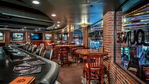 A bar area with multiple seating options, including bar stools and tables, and a brick wall with neon signage.