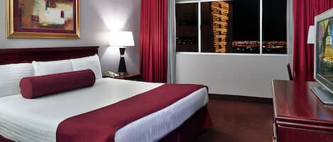 A hotel room with a large bed, a nightstand with a lamp, a painting on the wall, a window with a city view, and a TV on a wooden table.