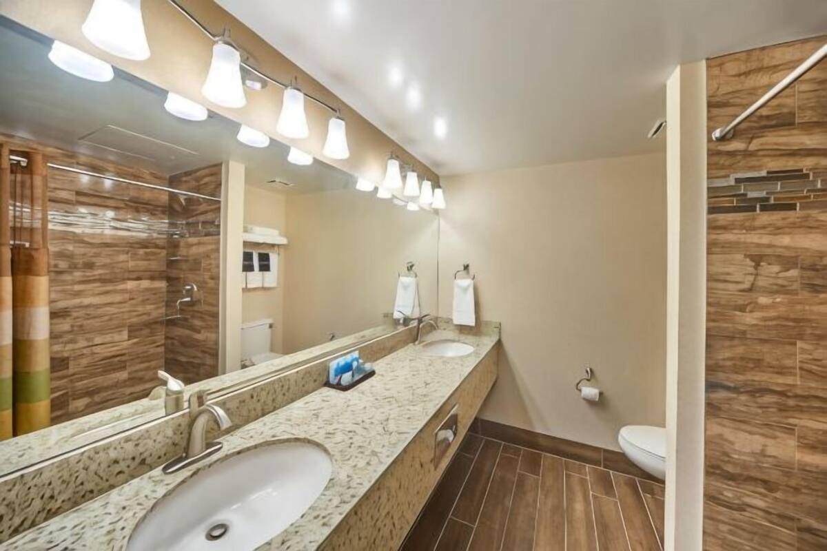 Een badkamer met een grote spiegel, twee wasbakken, een douche en een toilet.