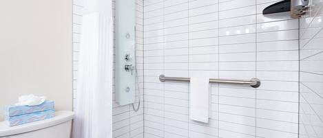 A modern bathroom with white tiles, a shower, a toilet, and a hand sanitizer dispenser.