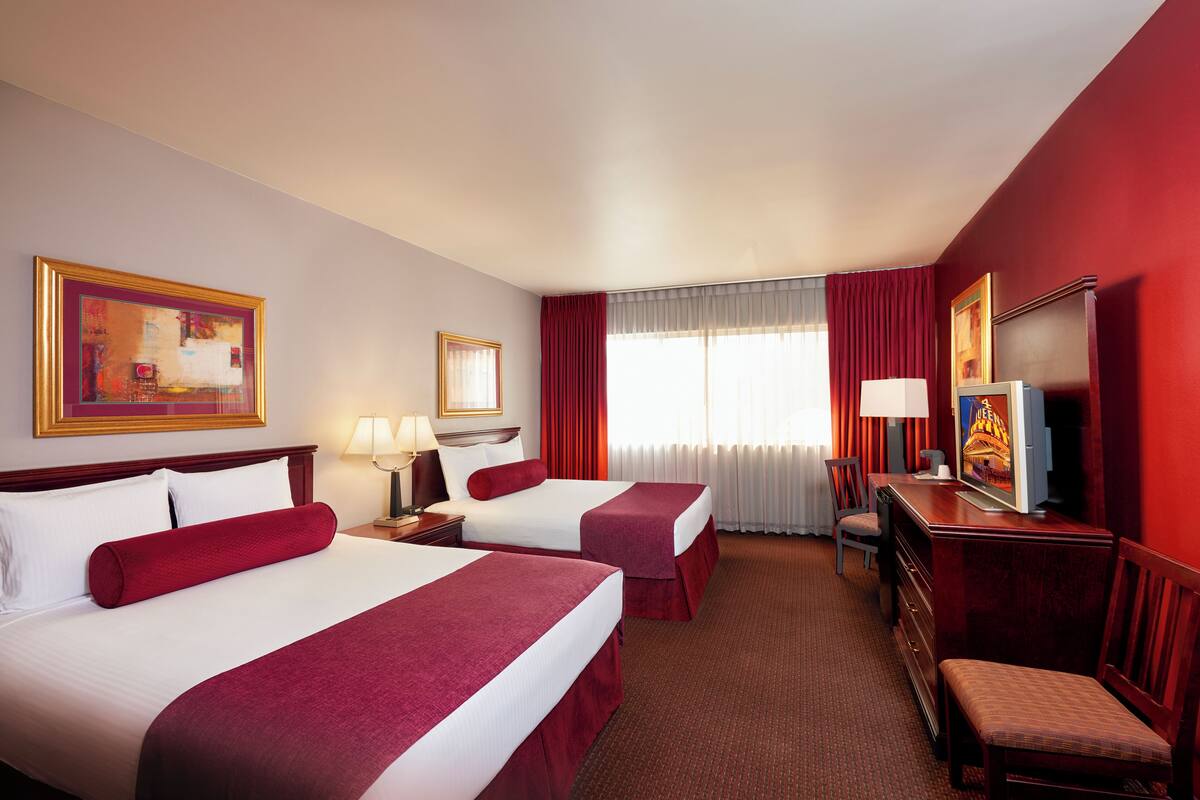Een hotelkamer met twee bedden, een bureau, een stoel, een televisietoestel en kunstwerken aan de muur.