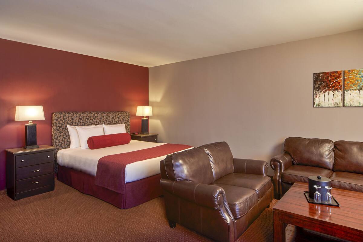 Een hotelkamer met een bed, twee nachtkastjes, een bruine leren bank, een houten salontafel en een schilderij aan de muur.