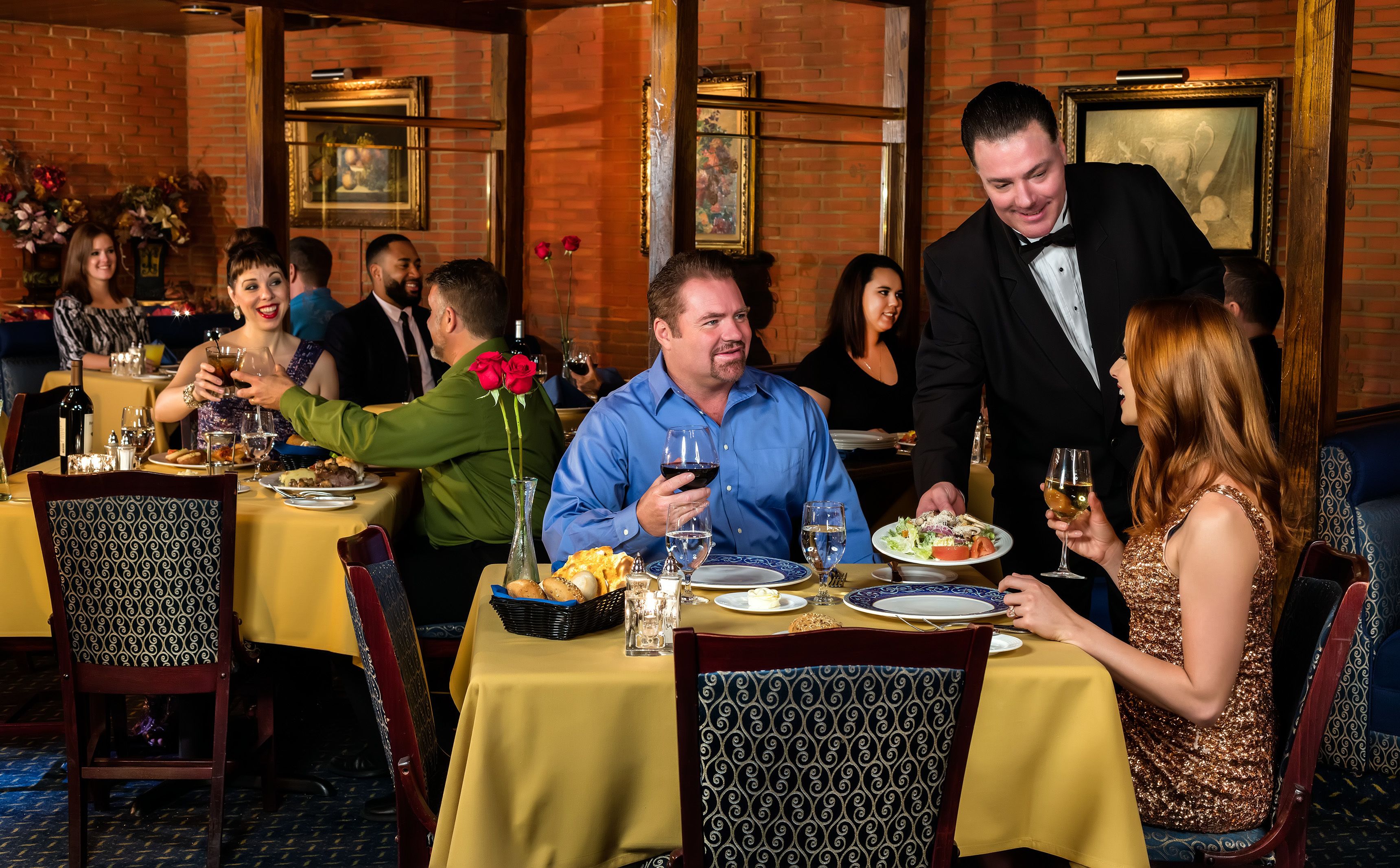 A restaurant with yellow tablecloths, patterned chairs, and framed artwork on the walls.