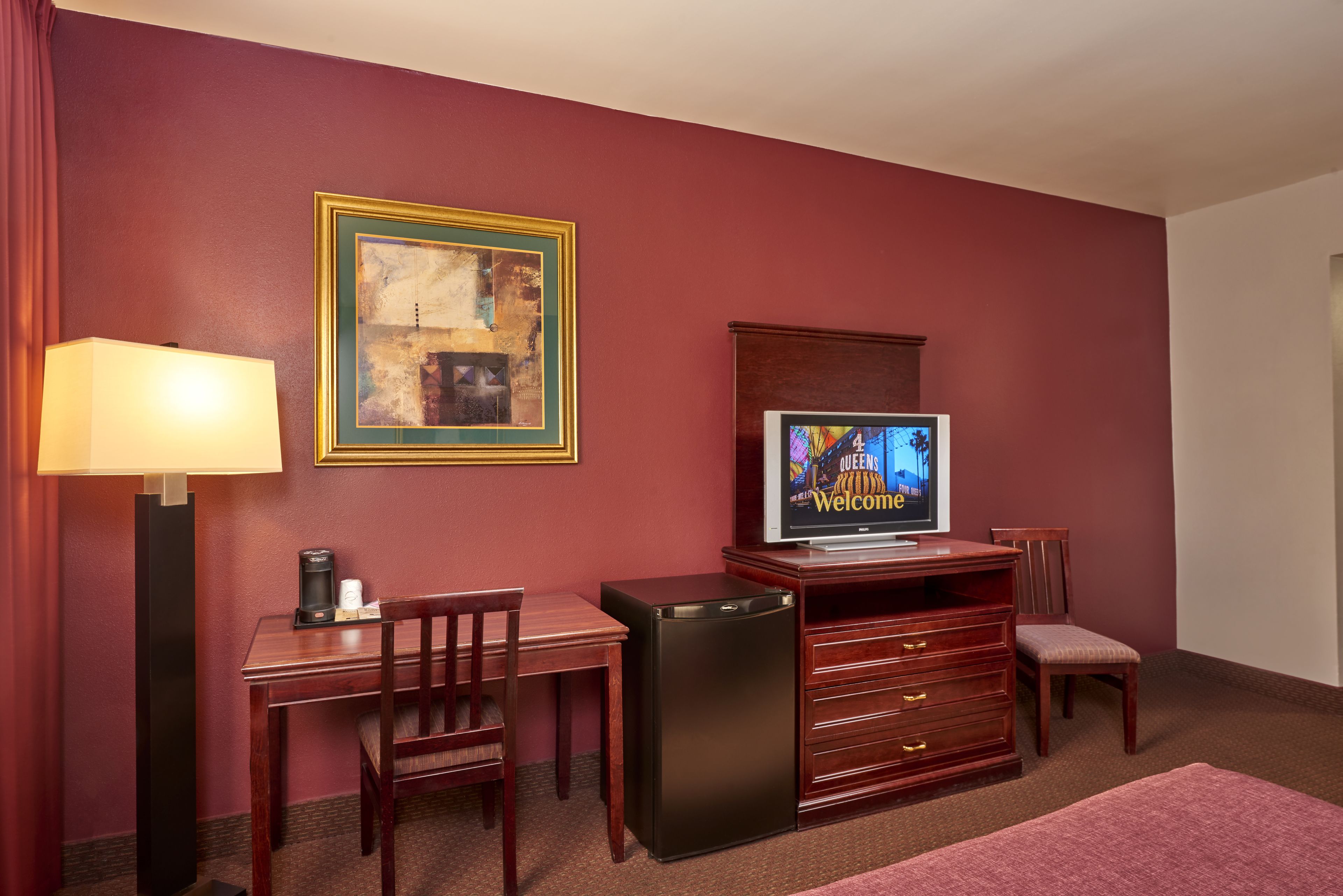 Ein Hotelzimmer mit Schreibtisch, Stuhl, Kühlschrank, Fernseher und einem kleinen Schrank.
