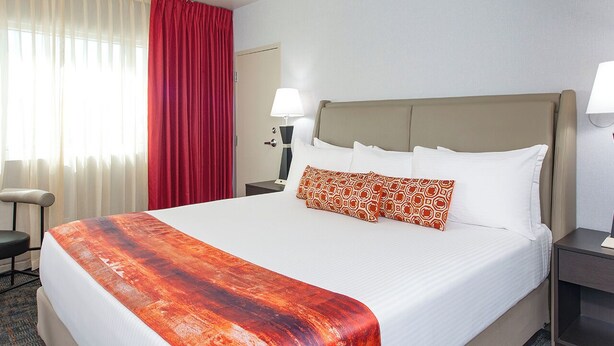 A hotel room with a large bed, a desk, a chair, a lamp, and a window with curtains.