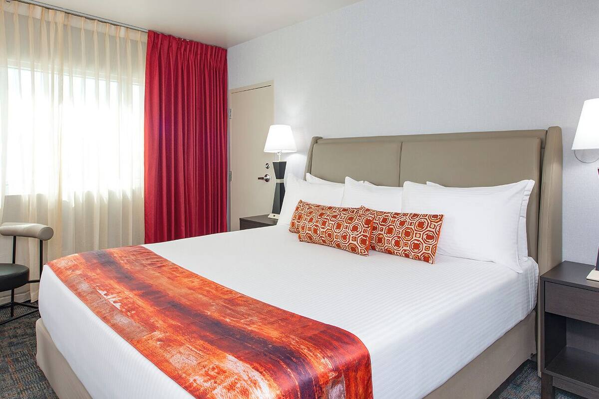 Hotelkamer met een groot bed, een bureau, een stoel, een lamp en een raam met gordijnen.