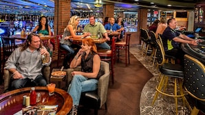 A bar area with multiple seating arrangements, a bar counter, and a variety of bottles and glasses on the shelves.