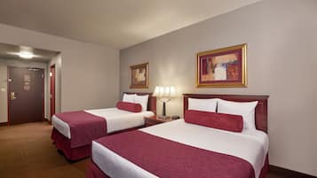 A hotel room with two beds, a door, a lamp, and two framed artworks on the wall.
