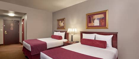 Habitación de hotel con dos camas, una puerta, una lámpara y dos cuadros en la pared.